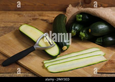 Sacco a sacco con molte zucchine fresche e asse di fette su sfondo di legno Foto Stock