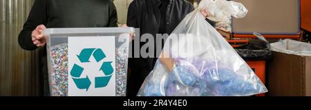 Vista ritagliata dei volontari che tengono il cestino con il cartello di riciclaggio e il sacchetto in una stazione di smaltimento dei rifiuti sfocata sullo sfondo, la cernita dei rifiuti e il riciclaggio Foto Stock