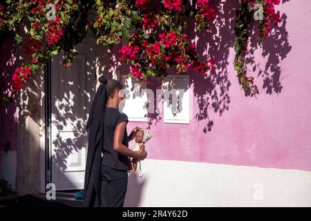 Bambino che tiene in mano una bambola davanti a un muro rosa con fiori di Bougainvillea Foto Stock