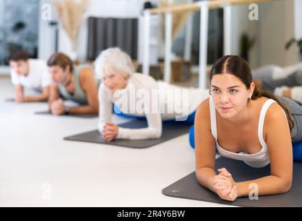 Donne e uomini che esercitano posizioni di yoga durante gli allenamenti di gruppo nel centro fitness, eseguendo stretching asana Urdhva Mukha Shvanasana Foto Stock