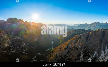 Le facce affilate delle alte montagne all'alba. Illuminato dai raggi del sole, le cime rocciose delle tre Cime di Lavaredo, sotto il cielo limpido e la vista aerea in controclit Foto Stock