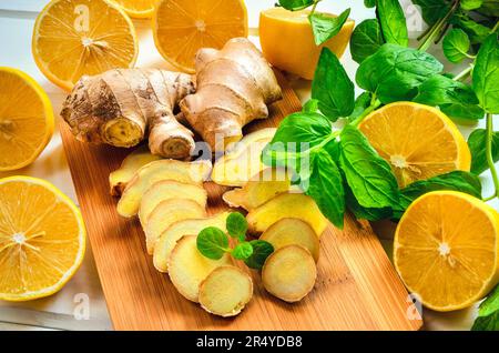 I limoni, zenzero e foglie di menta. Metà di limone, fette di zenzero e foglie di menta su una tavola di legno. Foto Stock