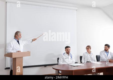 Dottore senior che tiene lezioni in sala conferenze con schermo di proiezione Foto Stock