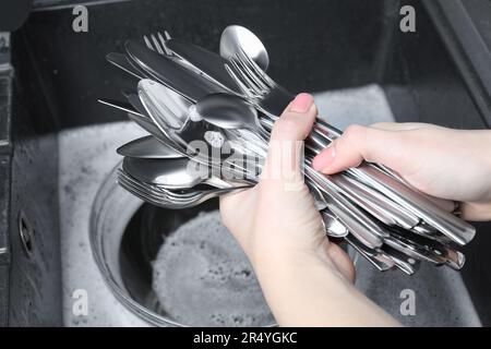 Donna che tiene utensili da cucina in argento pulito vicino al lavandino, primo piano Foto Stock