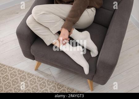 Donna in calze calde relax su poltrona a casa, primo piano Foto Stock
