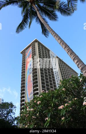 Honolulu, Hawaii, USA - 26 Maggio, 2023: Vista verticale della famosa torre dell'hotel Hilton Hawaiian Village, incorniciata da una palma e fiori di plumeria. Foto Stock