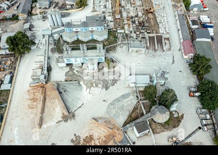 vista aerea dall'alto verso il basso dell'impianto di miscelazione del calcestruzzo. il deposito dell'impianto di dosaggio di calcestruzzo è riempito con vari mucchi di sabbia e ghiaia. Foto Stock