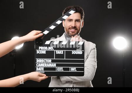 Attore che si esibisce mentre la seconda macchina fotografica dell'assistente tiene il clapperboard su sfondo nero Foto Stock