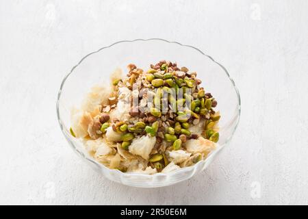 Una ciotola di vetro con pezzetti di pasta sfoglia e noci: Nocciole, mandorle e pistacchi per un delizioso dessert arabo umm ali o altro piatto su un leggero gr Foto Stock