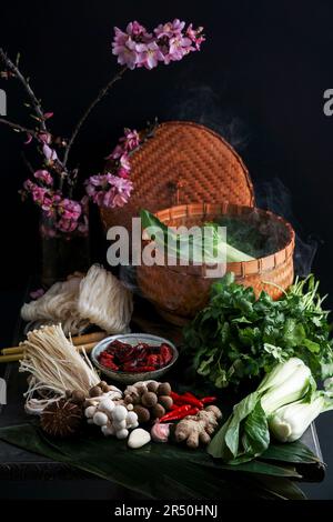 Ingredienti per la cucina asiatica in un vaporizzatore di bambù (tagliatelle di riso, funghi asiatici, shiitake, Shimeji, pak choi, foglie di bambù, zenzero, peperoncino) Foto Stock