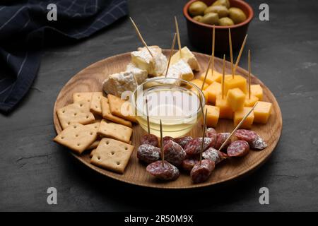 Stuzzichini da dentifricio. Pezzi di salsiccia, cracker e miele su tavola nera Foto Stock