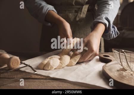 Donna che fa pane intrecciato a tavola di legno, primo piano. Tradizionale sfida Shabbat Foto Stock