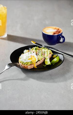 Smaschiare l'avocado con un uovo in camicia su pasta madre con caffè e succo d'arancia Foto Stock