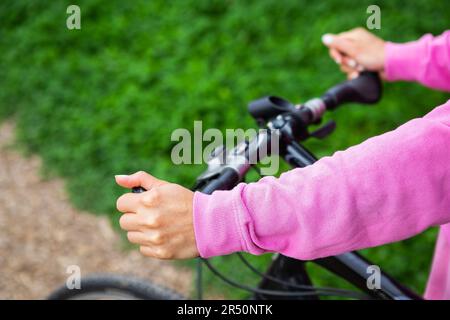 Una bambina in felpa rosa si tiene sul manubrio di una bicicletta, un giro in bicicletta nel parco. Le attività ricreative all'aperto sono buone per la salute Foto Stock