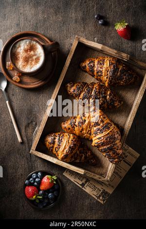 Croissant in un vassoio di legno con una tazza di caffè e frutti di bosco freschi su un tavolo di legno Foto Stock