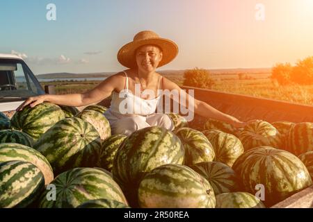 donna anguria. Si siede in un cappello su una montagna di cocomeri. Rimorchio con cocomeri nel mercato. Foto Stock