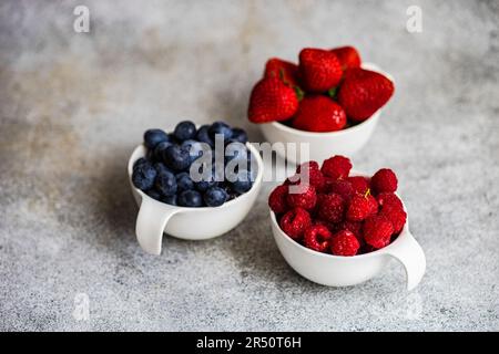 Ciotola con fragole sane, mirtilli e lamponi su tavola di cemento Foto Stock