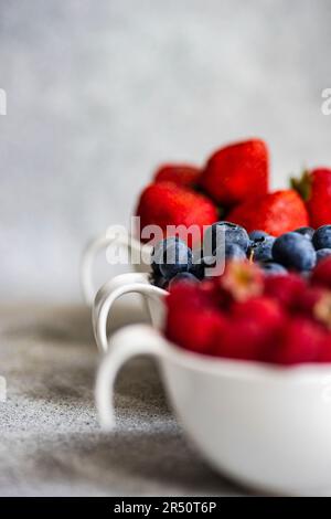 Fragole, mirtilli e lamponi in piccole ciotole su fondo di cemento Foto Stock