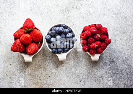 Fragole, mirtilli e lamponi in piccole ciotole su una base di cemento Foto Stock