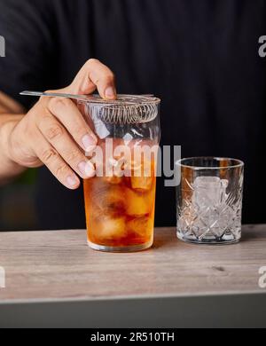 Preparare un cocktail vecchio stile, sforzando il cocktail Foto Stock