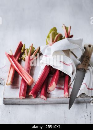 Rabarbaro lavato su un tagliere con un panno e un coltello Foto Stock