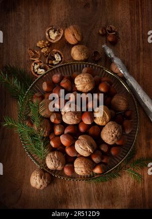Nocciole e noci con ciuffi di aghi di pino in una ciotola d'argento accanto a un rompigranella Foto Stock