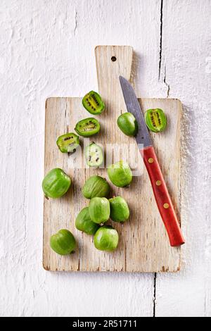 Bacche di Kiwi, intere e tagliate a metà, su tavola di legno Foto Stock