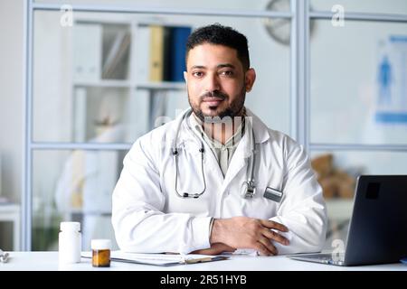 Ritratto del medico professionista che guarda la fotocamera mentre è seduto sul posto di lavoro in ufficio Foto Stock
