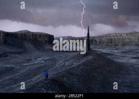 Vista posteriore di un turista irriconoscibile in piedi nella valle oscura di una grande gola, mentre ammirando la vista pittoresca delle montagne con fulmini Foto Stock