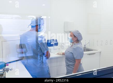 Vista laterale del dentista femminile in uniforme medica con vista posteriore del collega maschio con maschera protettiva in piedi e lavorando in clinica moderna Foto Stock