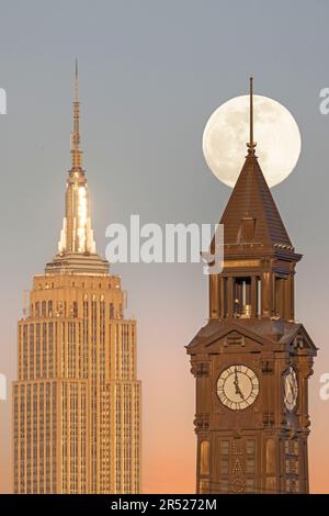 La luna piena sorge dietro la Torre dell'Orologio di Lackawanna a Hoboken, New Jersey, accanto all'iconico Empire state Building e al 1 Vanderbilt Foto Stock