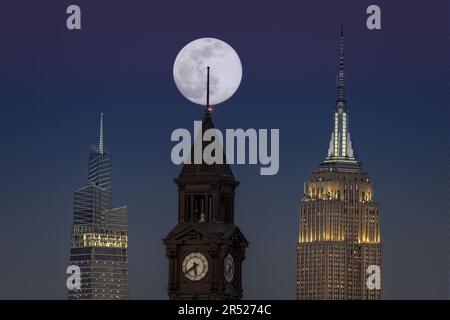 La luna piena sorge dietro la Torre dell'Orologio di Lackawanna a Hoboken, New Jersey, accanto all'iconico Empire state Building e al 1 Vanderbilt Foto Stock