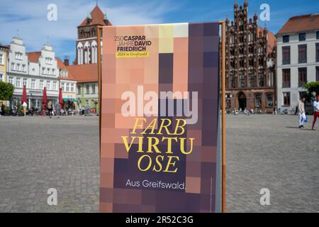 31 maggio 2023, Meclemburgo-Pomerania occidentale, Greifswald: Un espositore con l'iscrizione '250 anni di Caspar David Friedrich 2024 a Greifswald' si trova sul mercato. Oltre ad un vasto programma culturale, il 250th° anniversario della nascita del pittore Caspar David Friedrich nel prossimo anno lascerà tracce durature anche nella sua città natale di Greifswald. Le nuove finestre ad est della cattedrale saranno inaugurate il prossimo aprile. Secondo la città, l'anno di anniversario sarà cerimoniosamente aperto nella cattedrale già il 20 gennaio 2024. Già 160 eventi sono stati registi Foto Stock