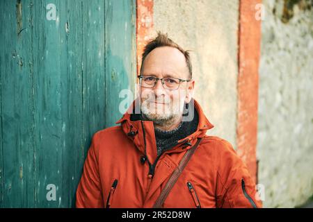 Ritratto all'aperto di un uomo di mezza età che indossa occhiali e giacca invernale arancione Foto Stock