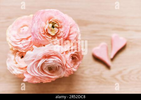 Bel bouquet di ranuncolo rosa con 2 cuori, vista dall'alto, sfondo in legno. Foto Stock