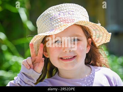 Giovane ragazza di 6 anni sorridente e che indossa un cappello da sole in una bella giornata calda in primavera nel Regno Unito Foto Stock