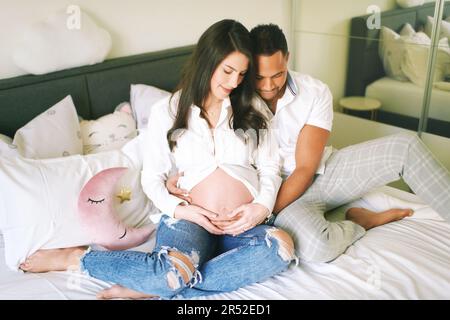 Ritratto interno di felice giovane famiglia, donna incinta con il suo marito amorevole rilassarsi a letto Foto Stock