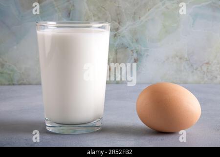 Bicchiere di latte e due uova su tavola blu, primo piano Foto Stock