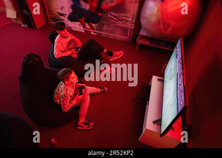 Due giocatori ragazzi giocano a calcio gamepad console di videogiochi nella sala giochi rossa. Foto Stock