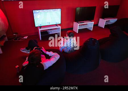 Due giocatori ragazzi giocano a calcio gamepad console di videogiochi nella sala giochi rossa. Foto Stock