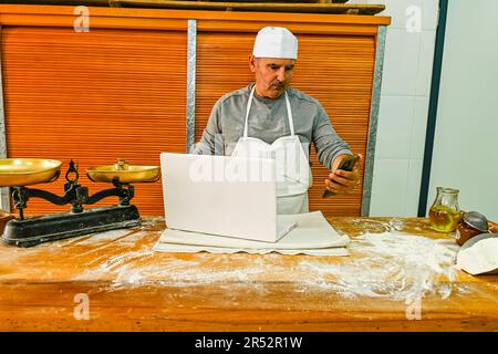 Baker consulenza sul computer, al tavolo di lavoro Foto Stock