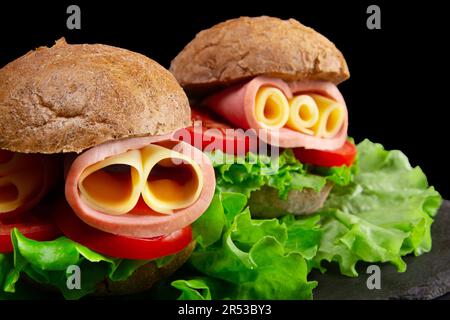 Primo piano di due panini con lattuga, pomodoro, prosciutto e formaggio isolati su sfondo nero Foto Stock