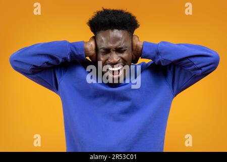 Il giovane africano urla, coprendo le orecchie di giallo Foto Stock