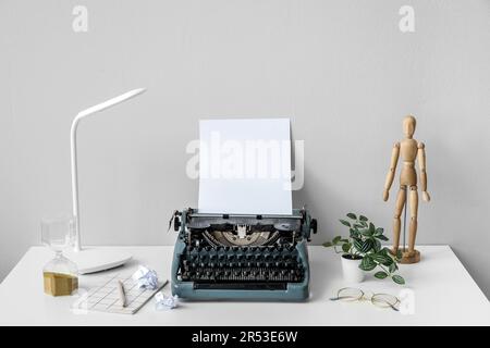 Macchina da scrivere vintage con manichino in legno, lampada e occhiali su tavolo bianco vicino alla parete Foto Stock