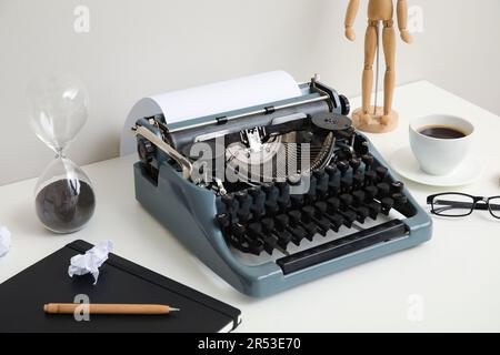 Macchina da scrivere vintage con tazza di caffè, manichino in legno e notebook su tavolo bianco vicino alla parete Foto Stock