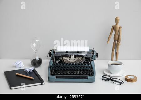 Macchina da scrivere vintage con tazza di caffè, manichino in legno e notebook su tavolo bianco vicino alla parete Foto Stock