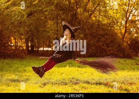 Una ragazza in costume da strega siede su una scopa galleggiante. Foto Stock