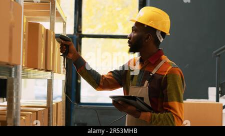 Il depot worker esegue la scansione delle scorte di carico con lo scanner del punto vendita, controllando la spedizione dell'ordine con il tablet. Dipendente del magazzino che si prepara alla distribuzione, che lavora nel settore manifatturiero. Scatto manuale. Foto Stock