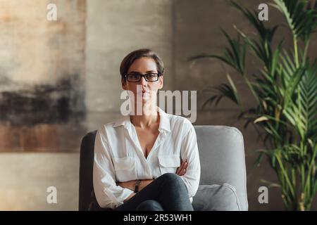 Donna fiduciosa seduta nel suo loft. Donna d'affari in occhiali e abbigliamento formale. Foto Stock