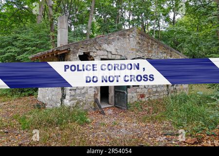 Casa di pietra abbandonata nel bosco con un nastro di polizia con scritto in esso 'cordone di polizia, non attraversare'. Foto Stock